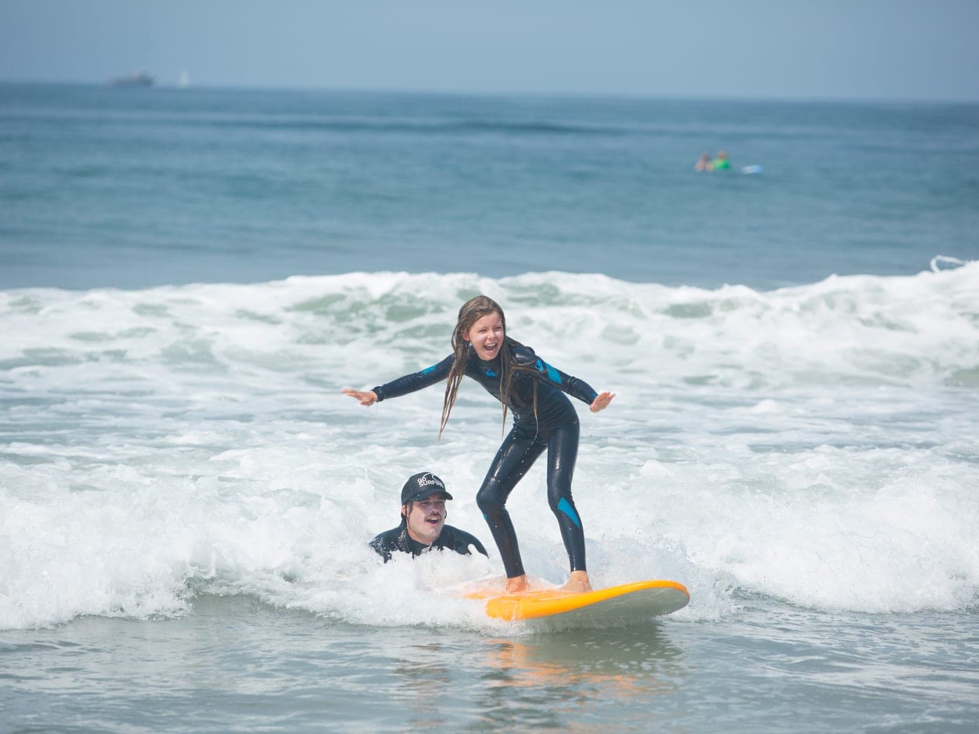 A BeachSports coach guiding a camper up onto a surfboard.