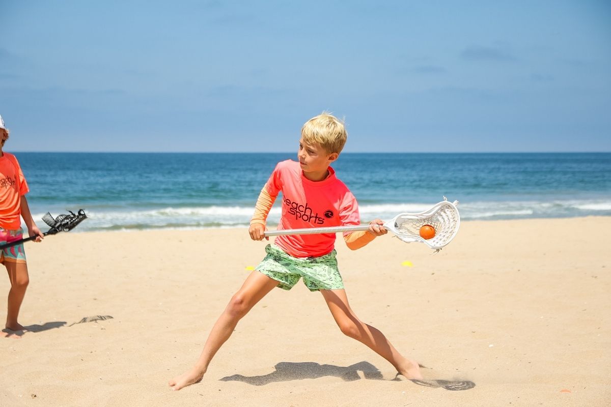 Beach Camp Lacrosse instructor teaching a summer beach camper how to play lacrosse