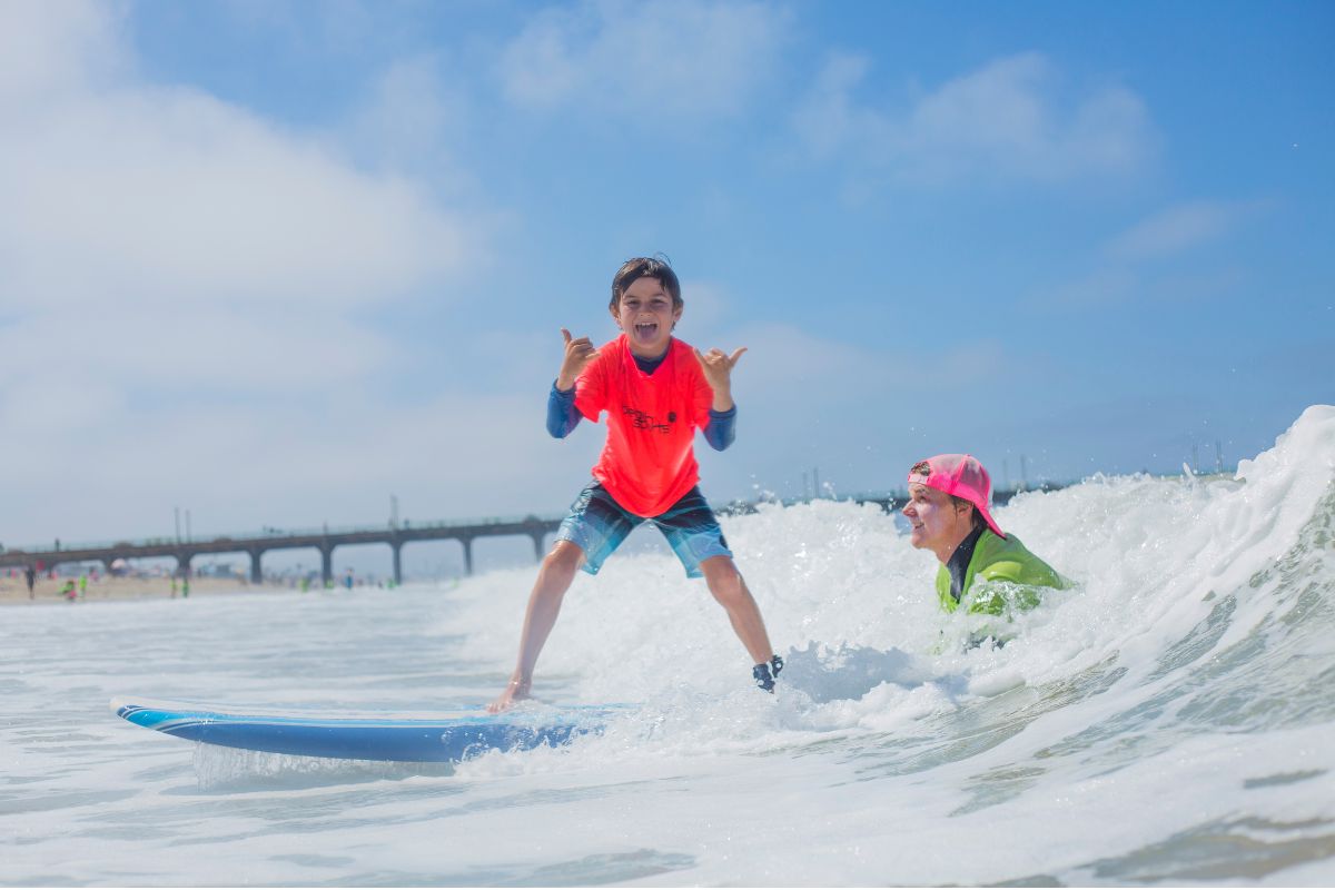 Surf camp logo over image of kids learning how to surf in Manhattan Beach